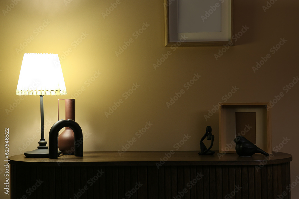 Glowing lamp, vase and decor on wooden table in dark room