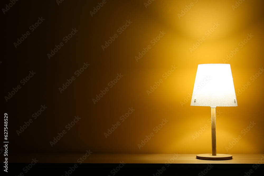 Glowing lamp on wooden table in dark room