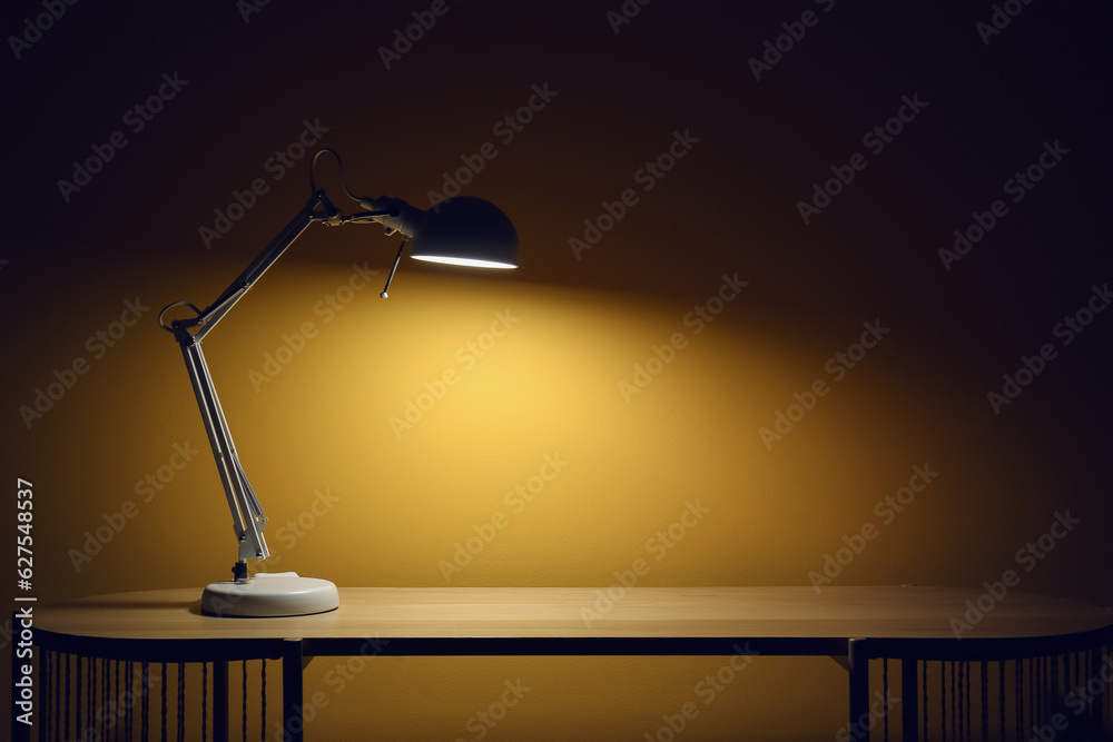 Glowing lamp on wooden table in dark room