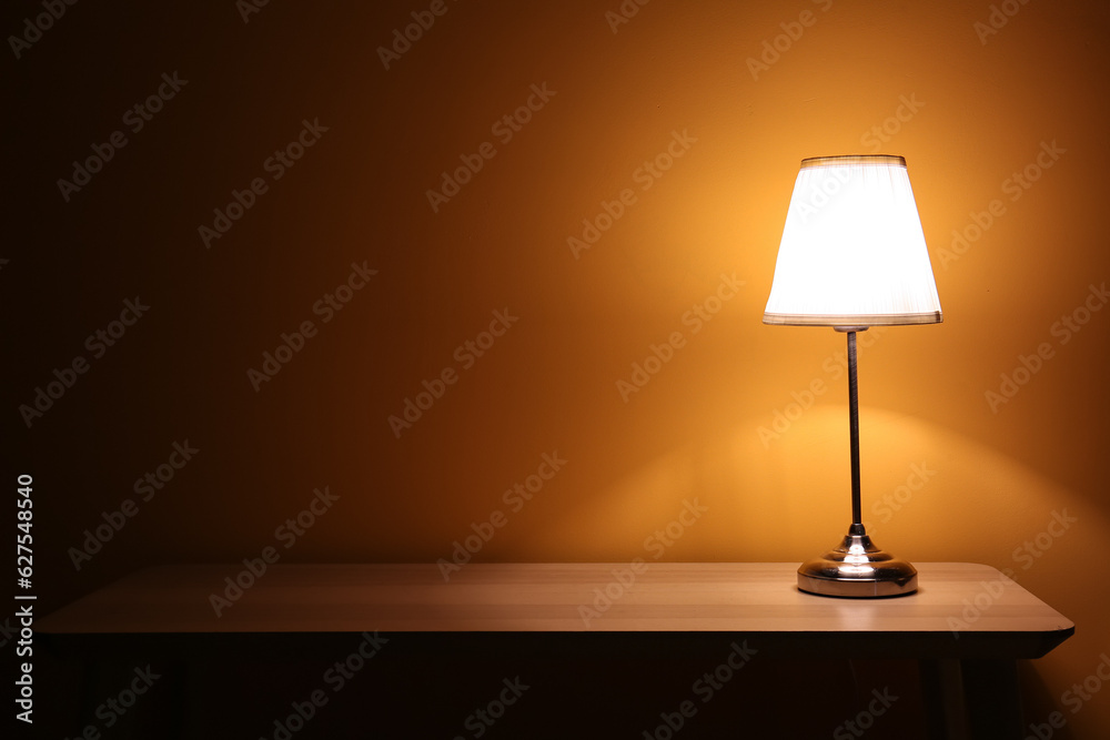 Glowing lamp on wooden table in dark room