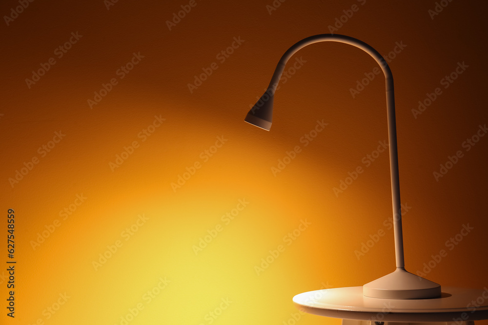 Glowing lamp on table near orange wall in dark room