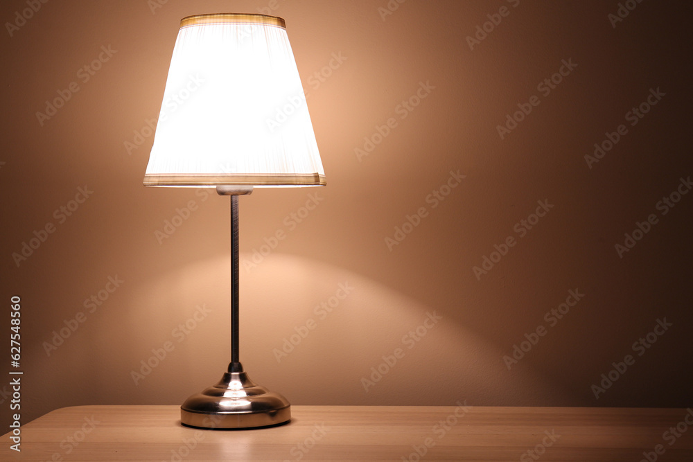 Glowing lamp on wooden table in dark room