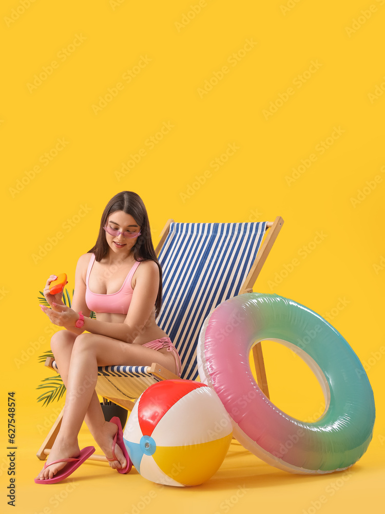 Young woman with sunscreen cream in deck chair on yellow background