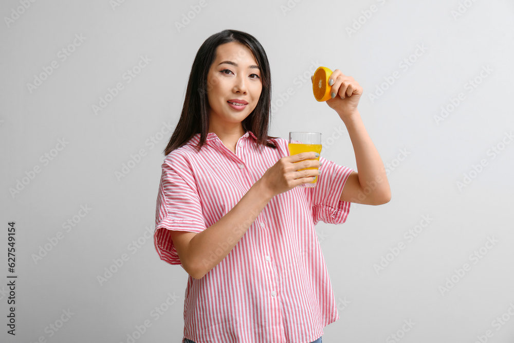 Beautiful Asian woman with orange and glass of juice on light background