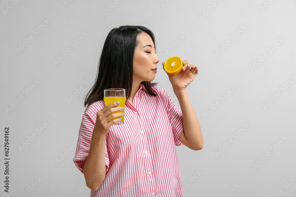 Beautiful Asian woman with orange and glass of juice on light background