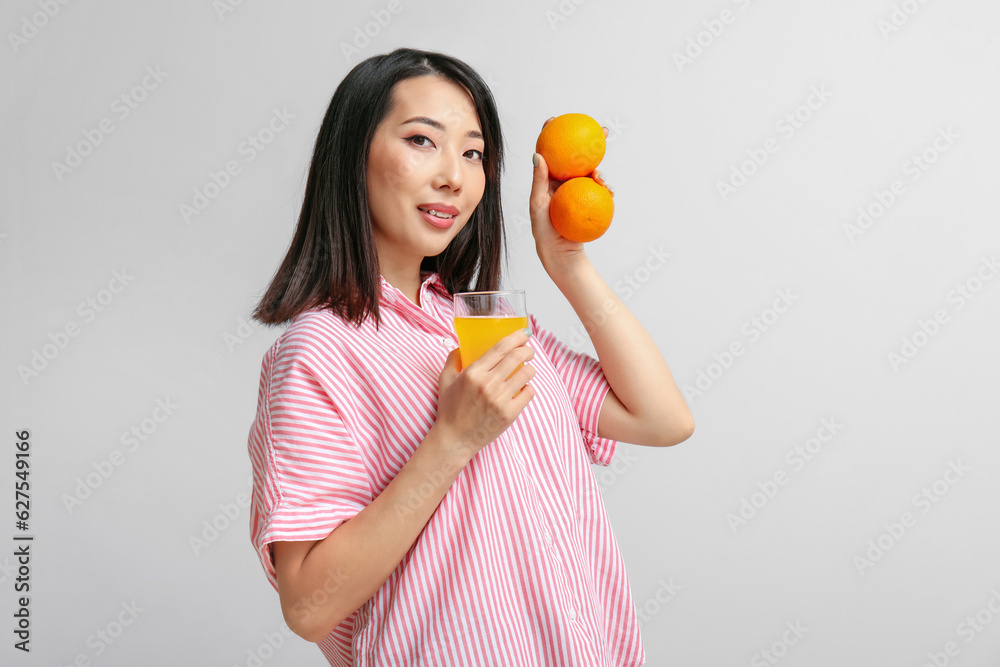 Beautiful Asian woman with oranges and glass of juice on light background