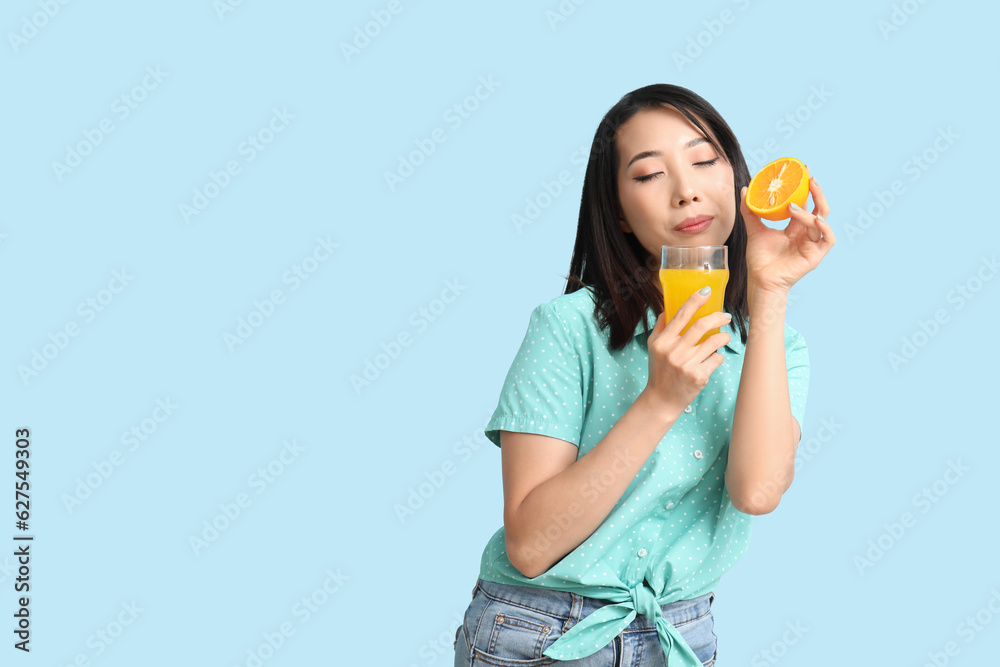 Beautiful Asian woman with orange and glass of juice on blue background