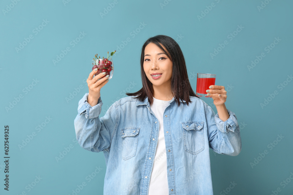 Beautiful Asian woman with cherries and glass of juice on blue background