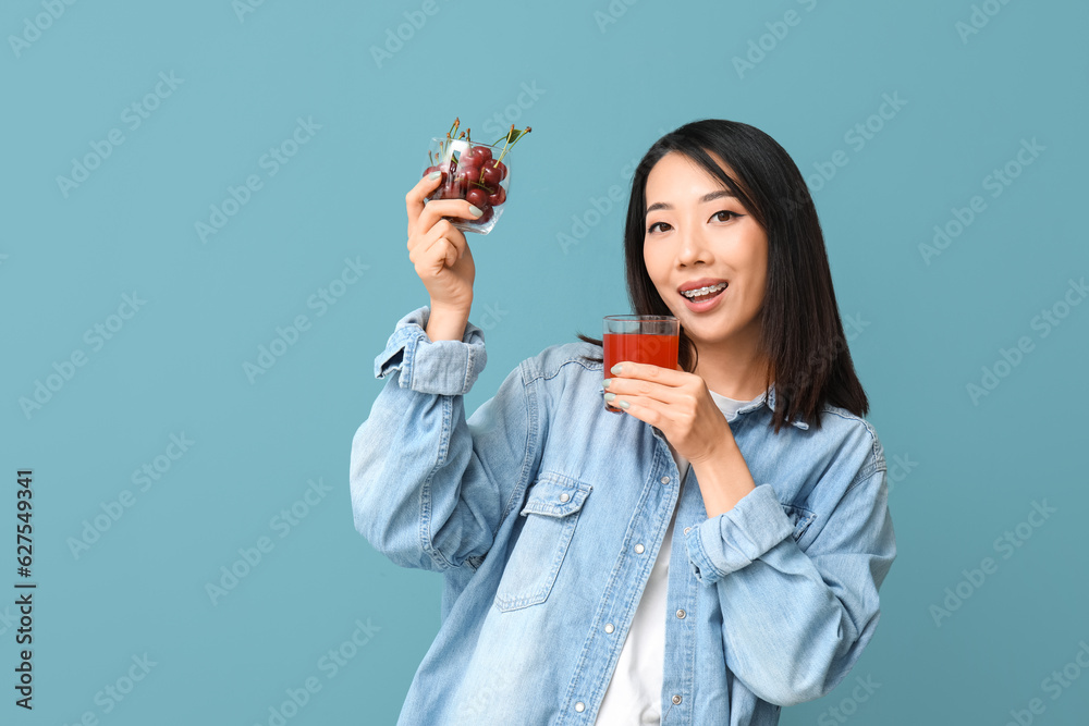 Beautiful Asian woman with cherries and glass of juice on blue background