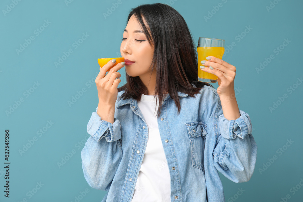 Beautiful Asian woman with orange and glass of juice on blue background