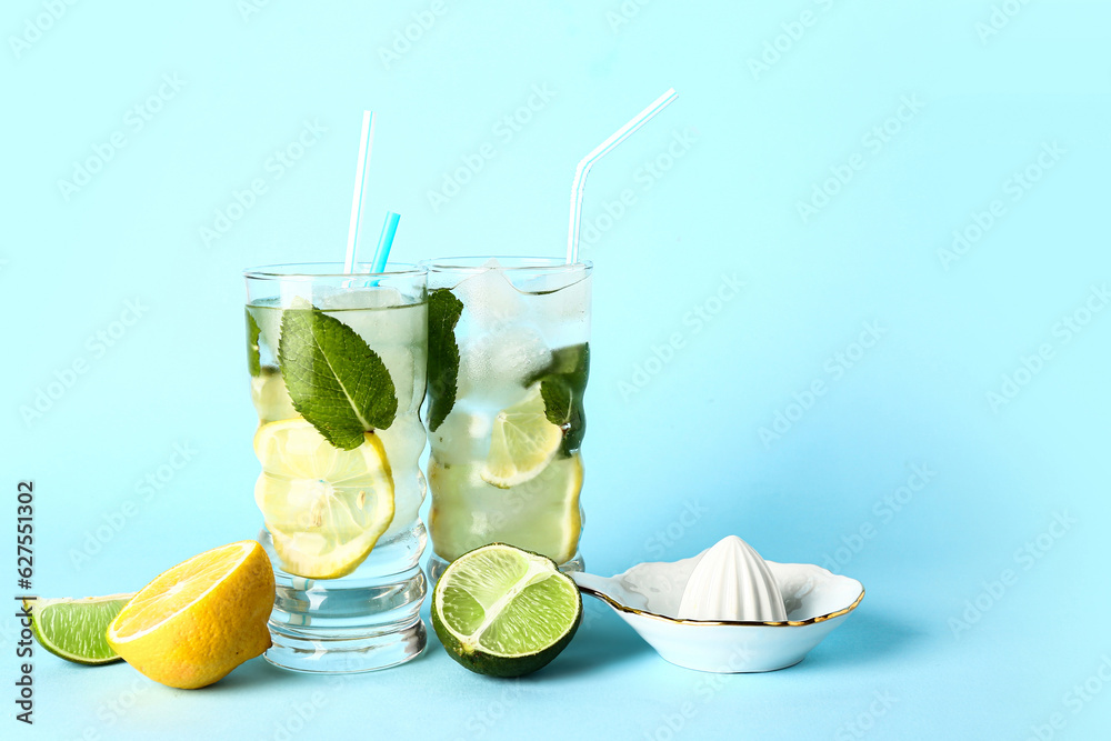 Glasses of fresh mojito, juicer and citrus fruits on color background