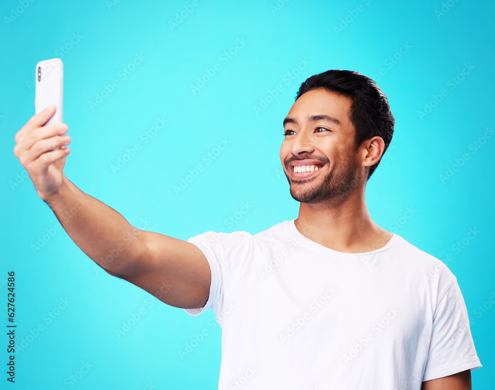 Asian man, selfie and smile in studio for social media post, web chat and excited by blue background