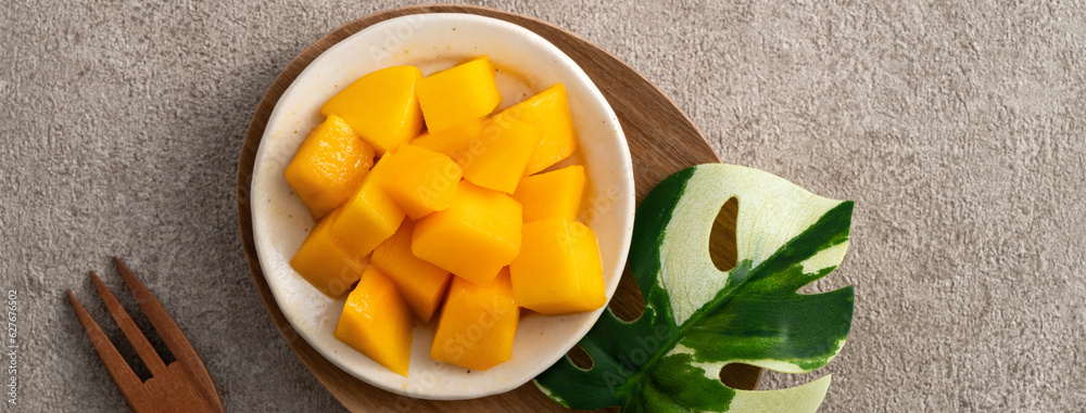 Fresh chopped, diced mango cubes on gray table background with tropical leaf.