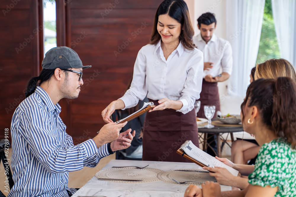 Asian waitress serving food to group of diverse customer in restaurant. 