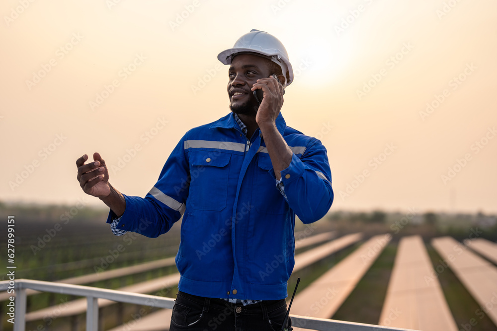 African young engineer talking on phone while work at solar cell field. 