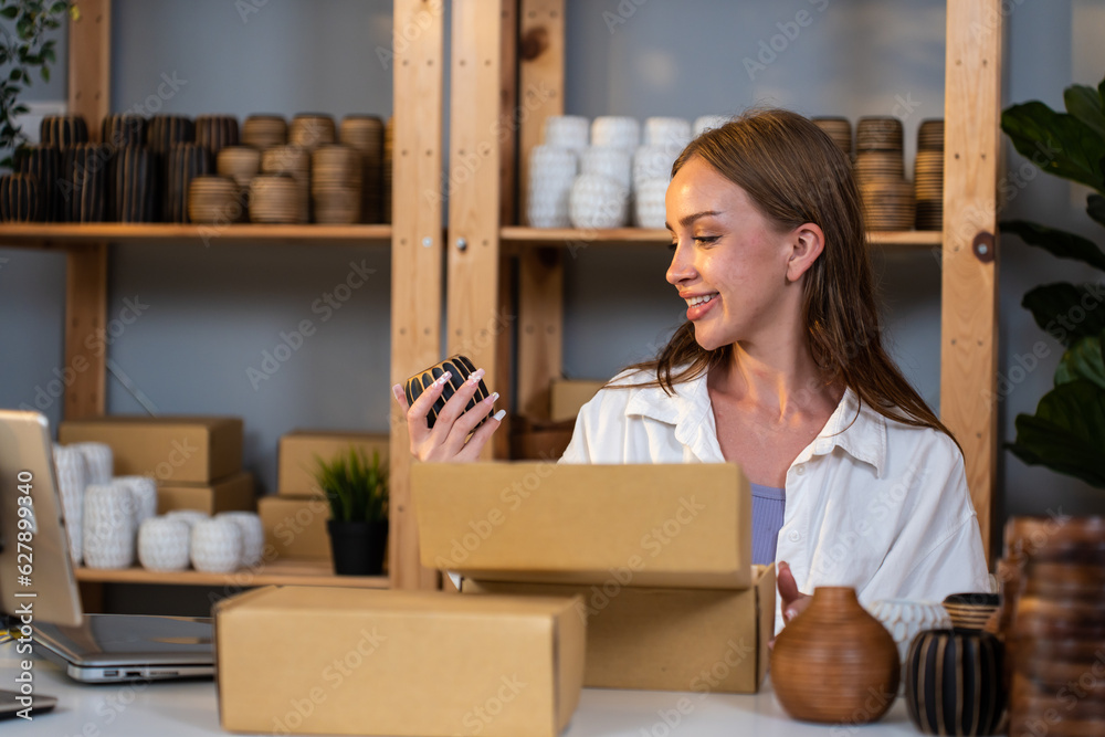 Caucasian young woman packing vase goods order into box for customer. 