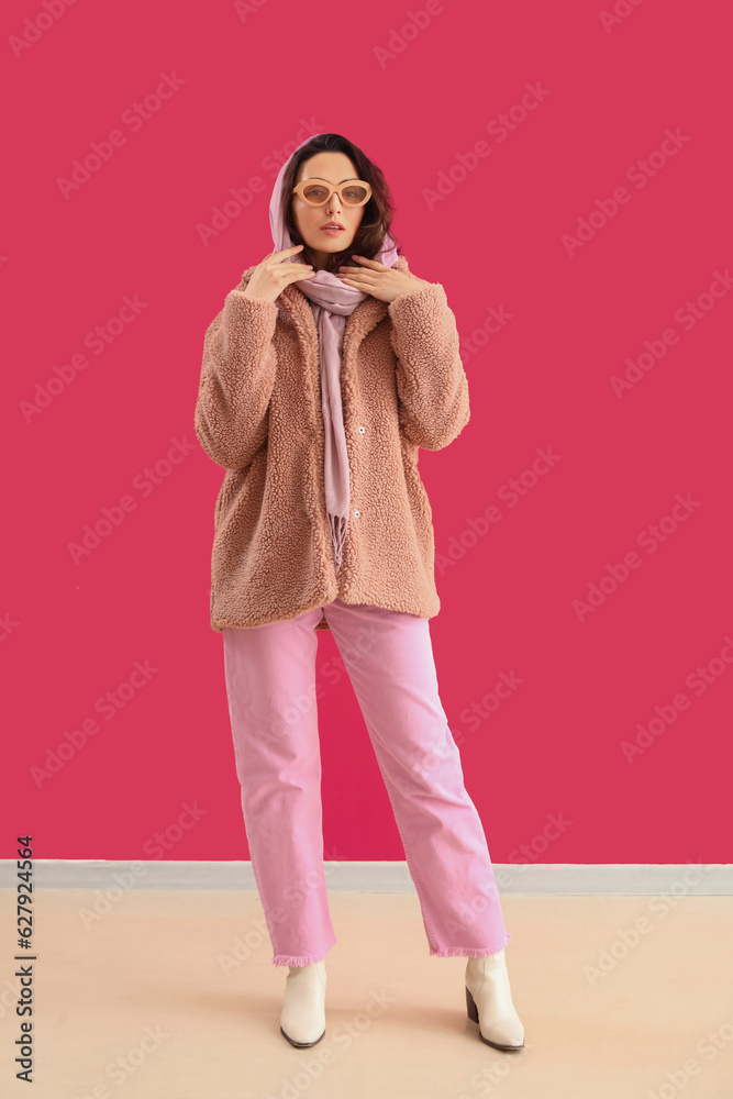 Stylish young woman in teddy coat and sunglasses near pink wall