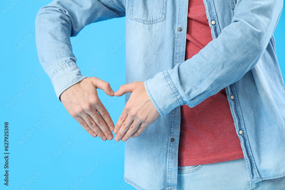 Young man making heart with his hands on light blue background, closeup