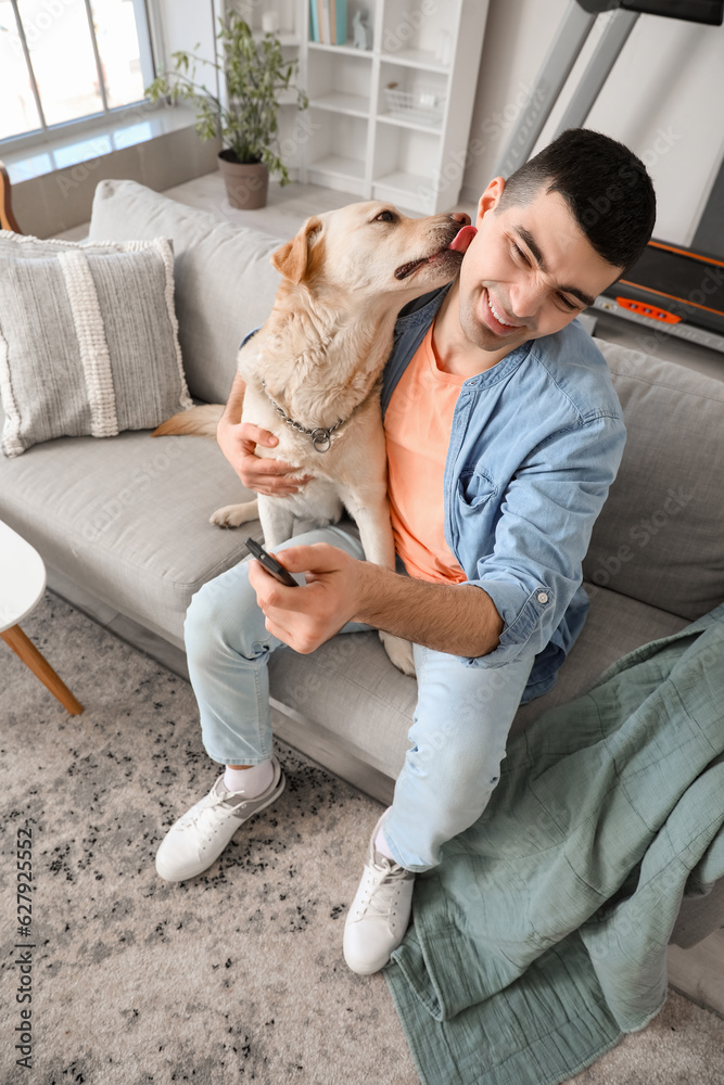 Young man with cute Labrador dog watching TV on sofa at home