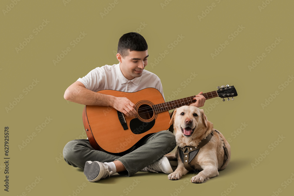 Young man with cute Labrador dog playing guitar on green background