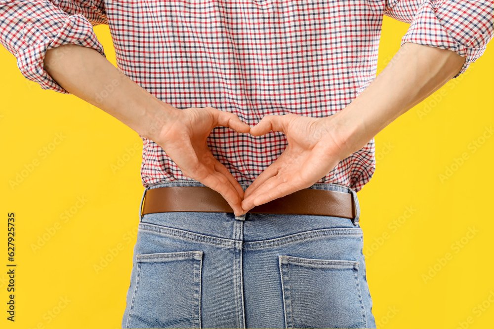 Handsome man making heart with his hands on yellow background, back view