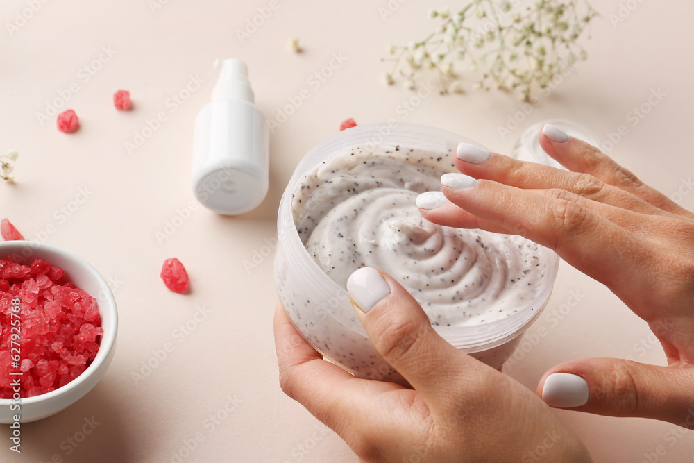 Female hands with jar of body scrub, cosmetic product and gypsophila flowers on color background, cl