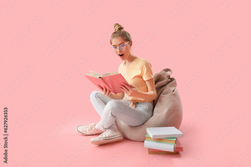 Surprised young woman reading book on pink background