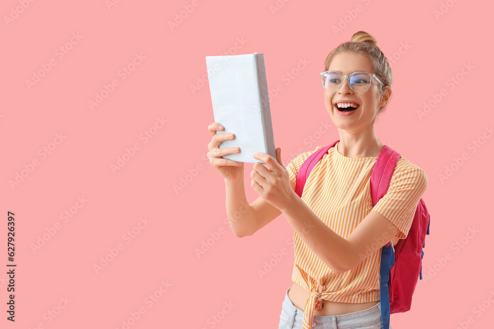 Happy female student with book on pink background