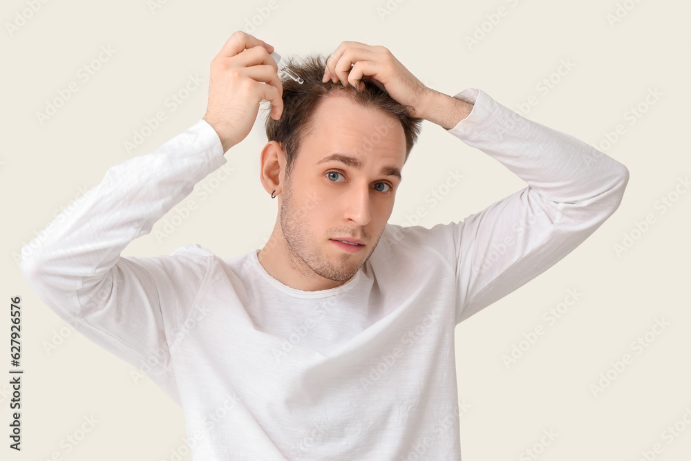 Young man using serum for hair growth on white background