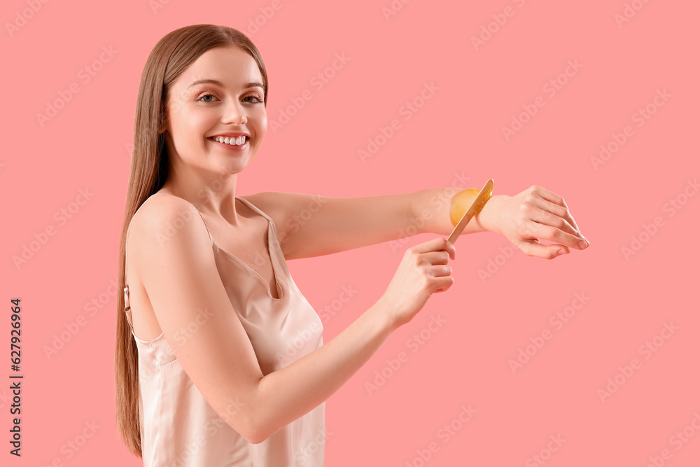 Young woman applying sugaring paste onto her arm against pink background