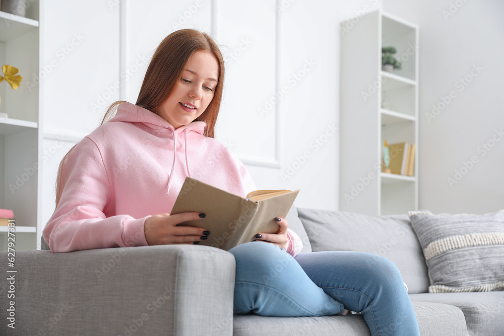 Teenage girl reading book on sofa at home