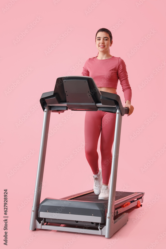 Sporty young woman training on treadmill against pink background