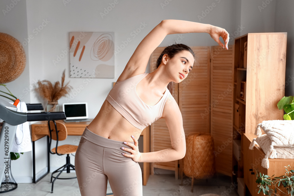 Sporty young woman training near treadmill at home