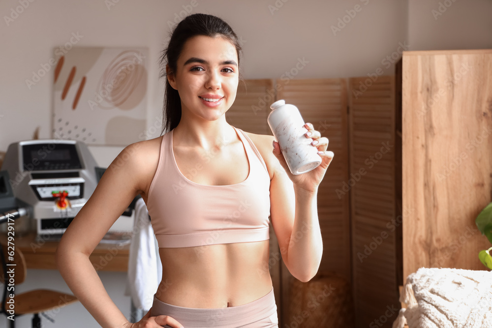 Sporty young woman with bottle of water after training on treadmill at home