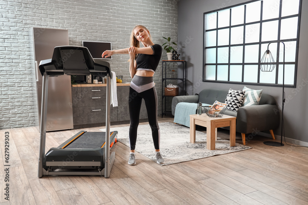 Sporty young woman training near treadmill at home