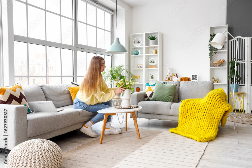 Beautiful young woman sitting on cozy sofa near big window in living room