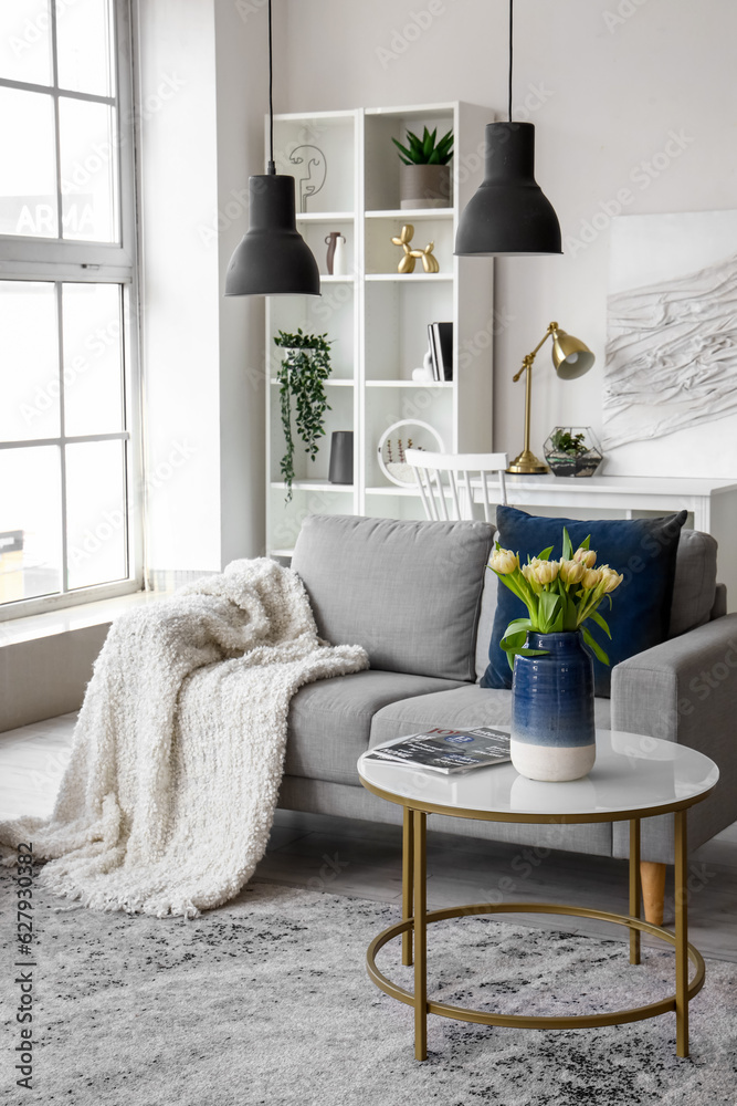 Vase with beautiful tulip flowers and magazines on coffee table in living room