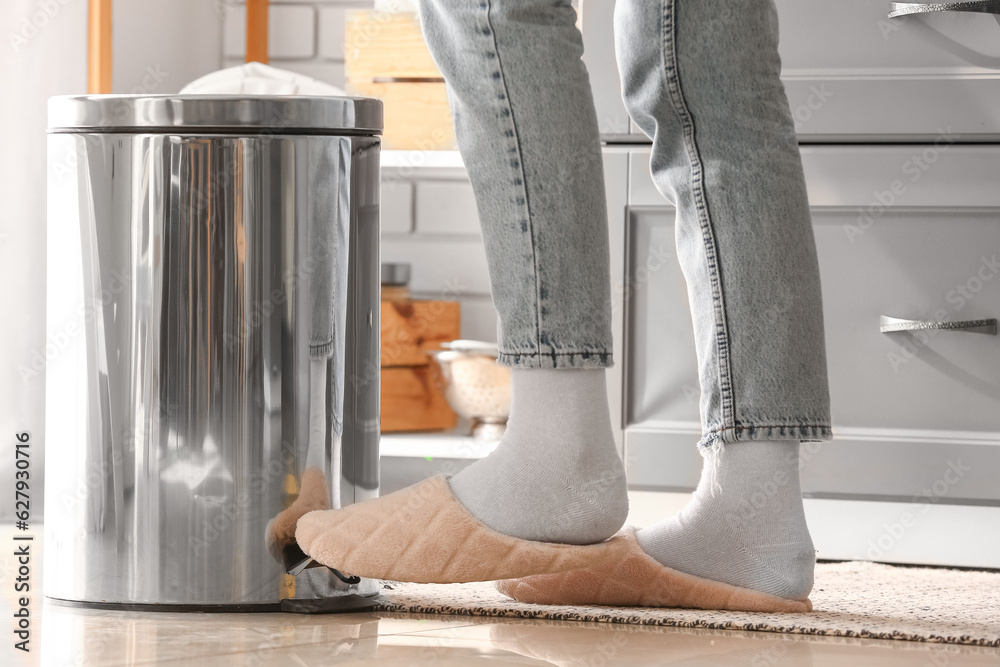 Woman opening trash bin with her foot in modern kitchen