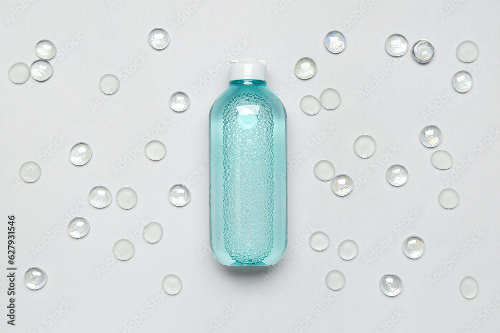 Bottle of micellar water with glass stones on light background