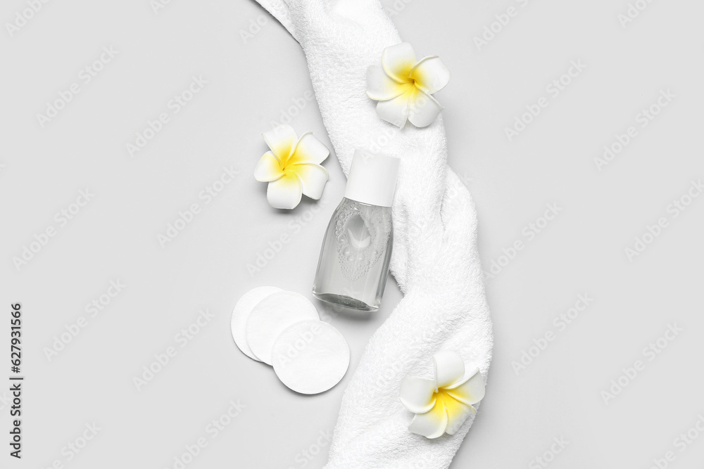 Bottle of micellar water with cotton pads, flowers and towel on light background