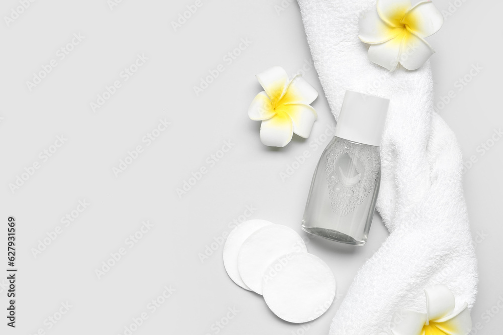 Bottle of micellar water with cotton pads, flowers and towel on light background