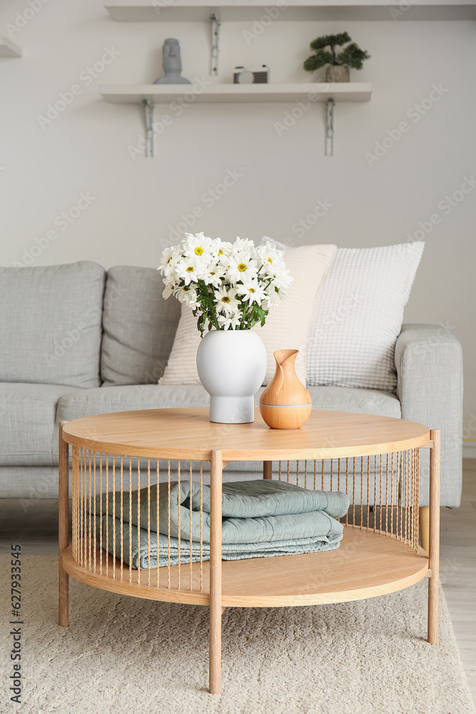 Vase with blooming chrysanthemum flowers on wooden coffee table in interior of living room