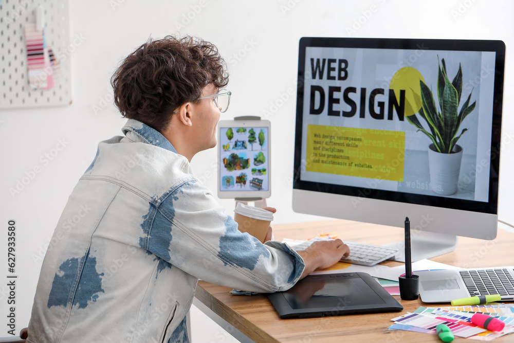 Male graphic designer with cup of coffee working at table in office