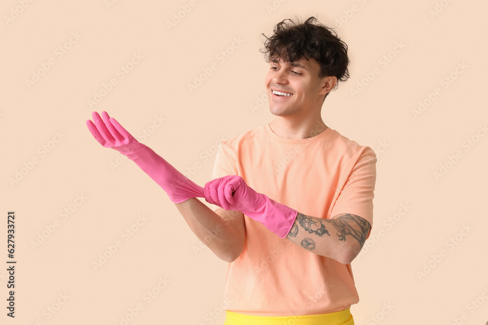 Young man putting rubber gloves on beige background