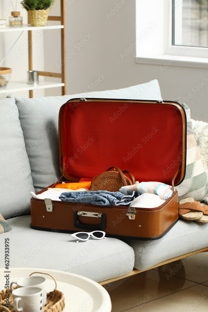 Open suitcase with female clothes on sofa in living room