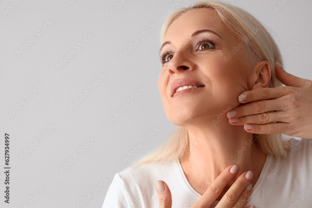 Mature woman doing face building exercise on light background, closeup