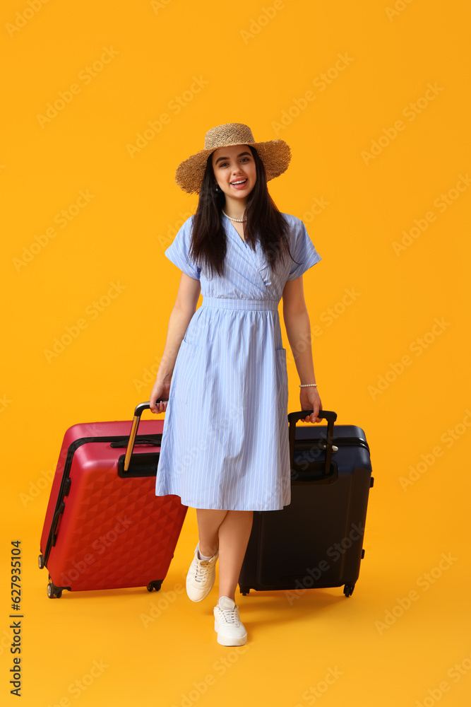 Young woman with suitcases on yellow background