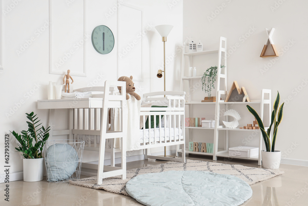 Interior of light bedroom with baby crib, changing table and shelving unit