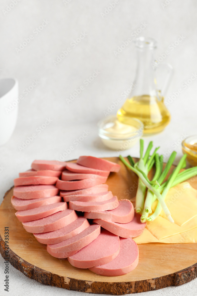 Wooden board with tasty sliced boiled sausage and cheese on light background