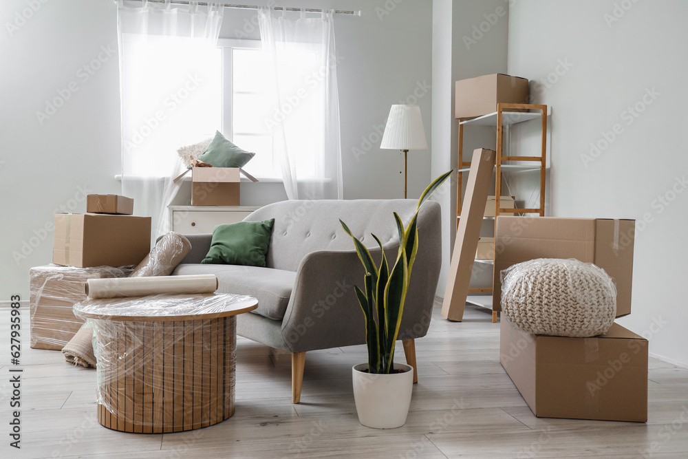 Sofa with wrapped table and cardboard boxes in living room on moving day